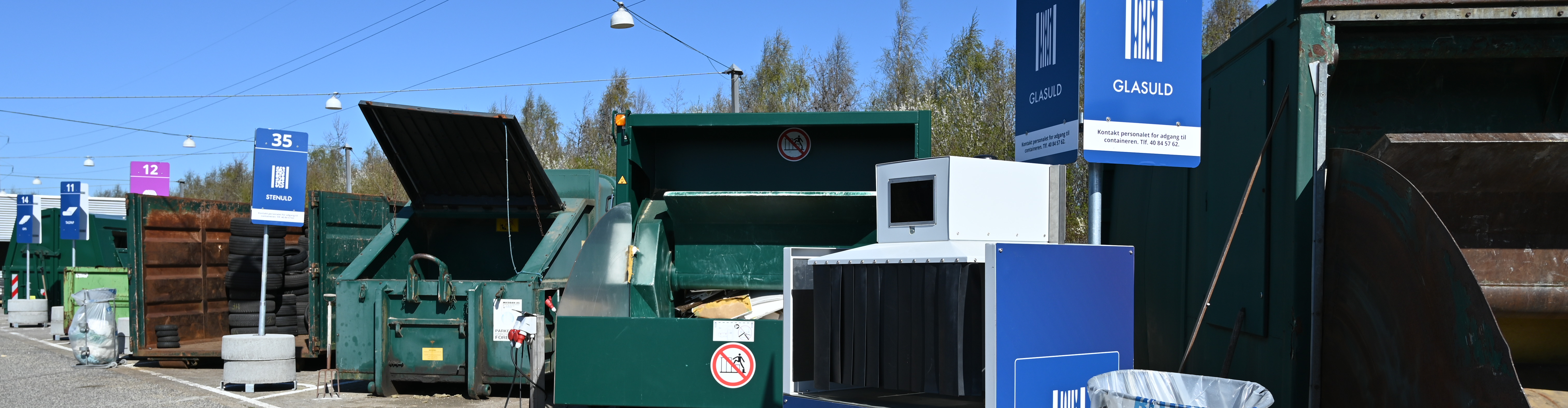 Skilte af stenuld og glasuld på genbrugspladsen står ved siden af grønne containere