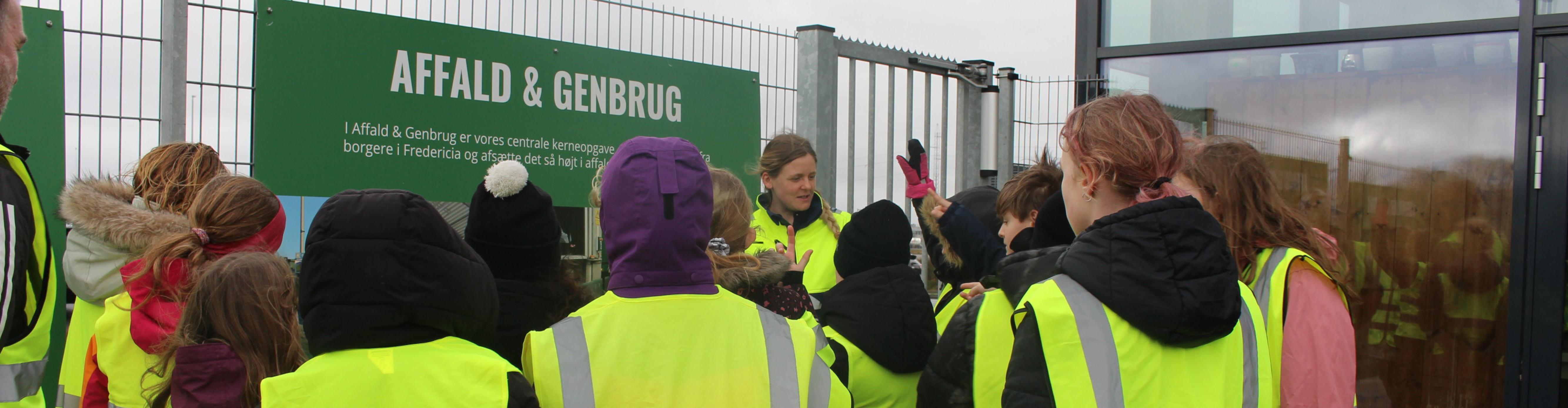 Skolelever står foran formidlingsskilt på genbrugspladsen sammen med medarbejder fra Affald & Genbrug